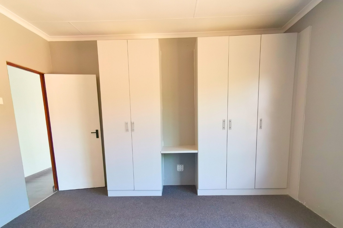 A clean, empty bedroom featuring neutral walls, carpeted flooring, and extensive built-in cabinetry with an integrated desk space.