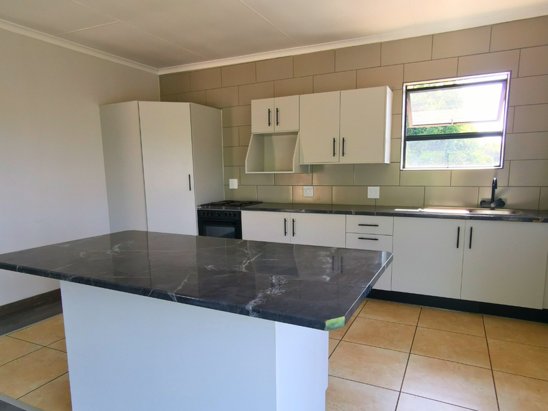 A clean, empty kitchen featuring modern white cabinetry, a dark stone-topped island, built-in oven, and tiled backsplash, offering a functional and neutral workspace.