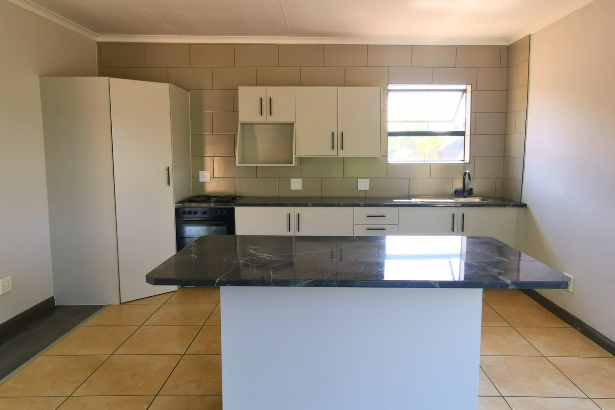 A clean, modern kitchen featuring a central island, built-in cabinetry, stone countertops, and integrated appliances, finished with neutral tiling.