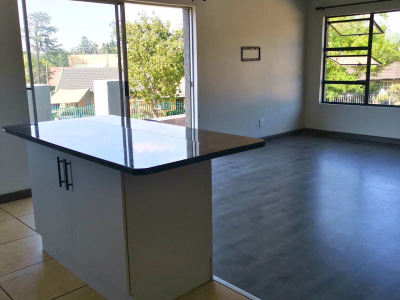 Spacious open-plan living area featuring a modern kitchen island, dual-tone flooring, and large windows providing ample natural light and access to a balcony.
