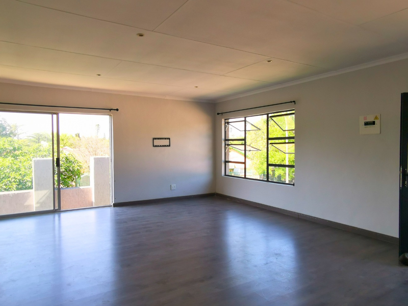 Spacious open-plan living area featuring dark laminate flooring, large windows, and a sliding door leading to an outdoor space.