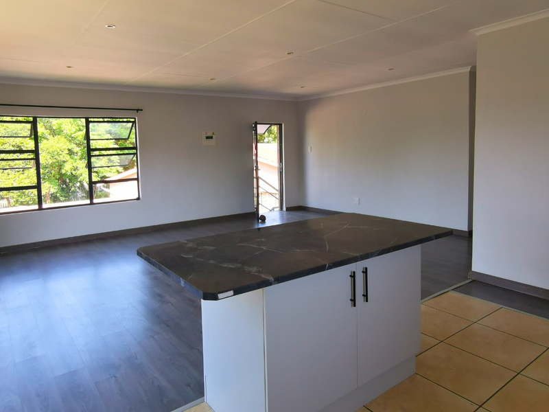 Spacious open-plan living area featuring a central kitchen island, a mix of laminate and tiled flooring, and large windows providing natural light.