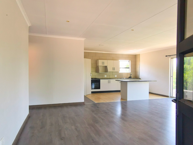Spacious open-plan living area featuring a modern kitchen with built-in cabinetry, an island, and laminate flooring, leading to an outdoor space.