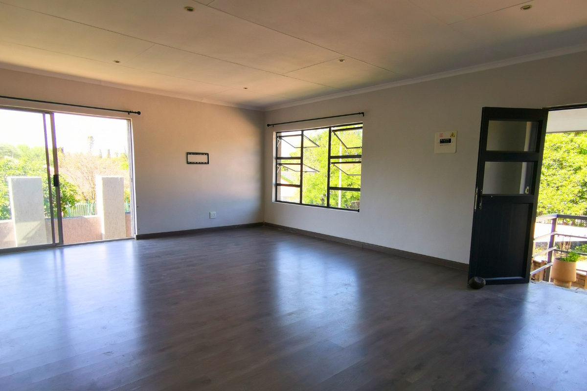 A spacious, empty living room featuring dark laminate flooring, large sliding glass doors, and ample natural light, providing a versatile blank canvas.