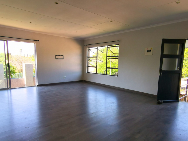 A spacious, empty living room featuring dark laminate flooring, large sliding glass doors, and ample natural light, providing a versatile blank canvas.