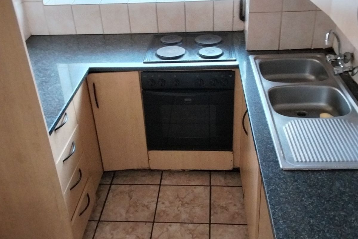 Compact kitchen featuring built-in oven, electric hob, double stainless steel sink, and laminate countertops with tiled splashback.