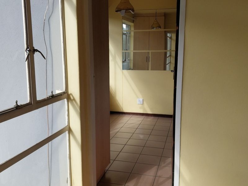 A vacant hallway featuring tiled flooring, built-in storage cupboards, and metal-framed windows, presenting a dated interior space ready for renovation.