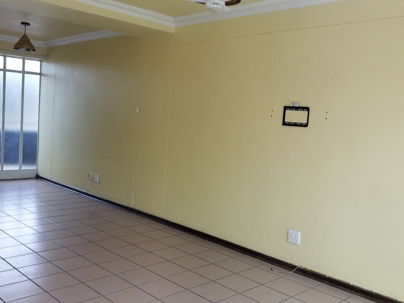 An empty living room featuring tiled flooring, neutral yellow walls, ceiling cornice, and a glass panel door leading to an exterior space.