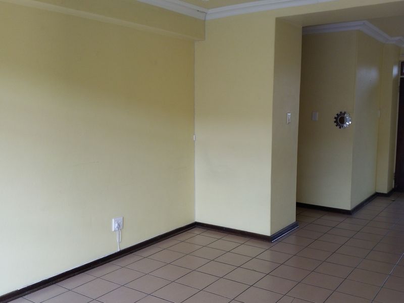 An empty living area featuring tiled flooring, neutral yellow walls, and a direct entrance door, providing a blank canvas for interior design.