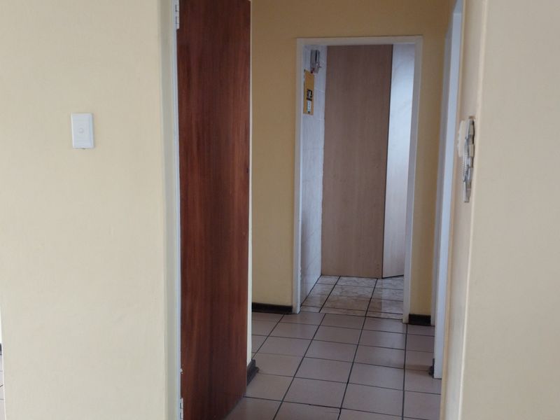 A functional hallway featuring tiled flooring, a wooden door, and an intercom system, providing access to other areas of the flat.