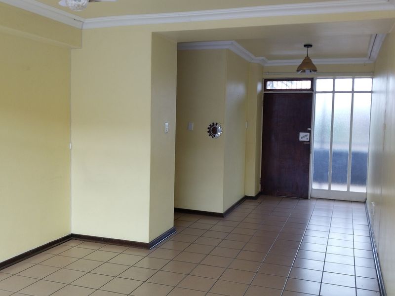 An empty, open-plan living area featuring tiled flooring, neutral yellow walls, and direct access to an exterior entrance.