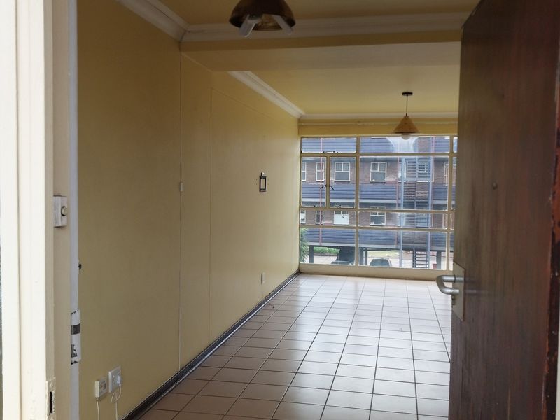 An empty, open-plan living area featuring tiled flooring, large windows providing natural light, and neutral wall finishes.