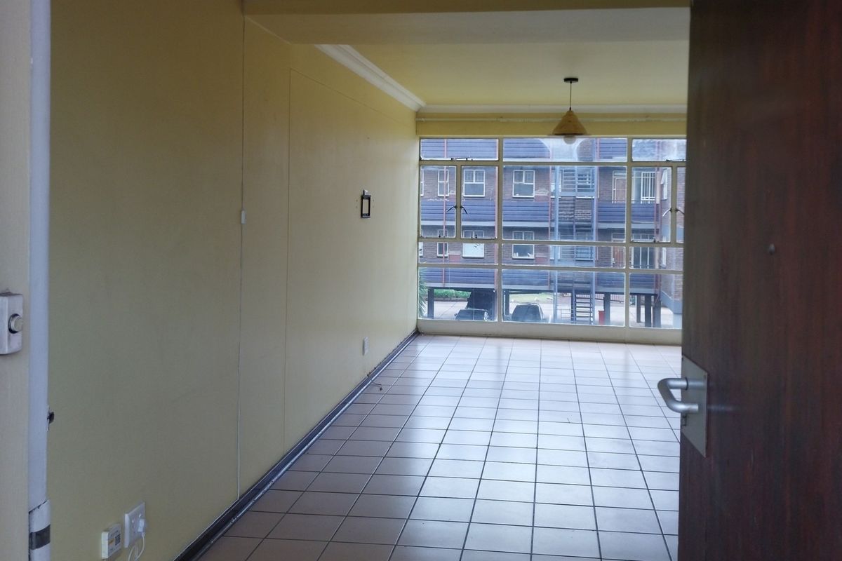 An empty, open-plan living area featuring tiled flooring, large windows providing natural light, and neutral wall finishes, ready for personalization.