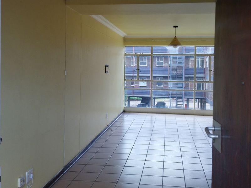 An empty, open-plan living area featuring tiled flooring, large windows providing natural light, and neutral wall finishes, ready for personalization.