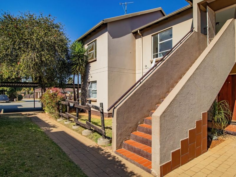 Exterior view of a flat featuring an external staircase with tiled treads, a paved walkway, and a timber fence leading to the entrance.