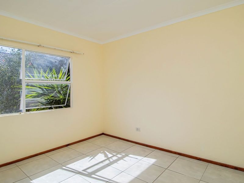 A vacant bedroom featuring neutral walls, tiled flooring, and an aluminium window frame, offering a blank canvas for personalization.
