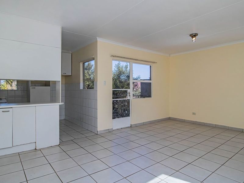 An open-plan living and kitchen area featuring tiled flooring, built-in cabinetry, and direct access to an outdoor space through a glass panel door.