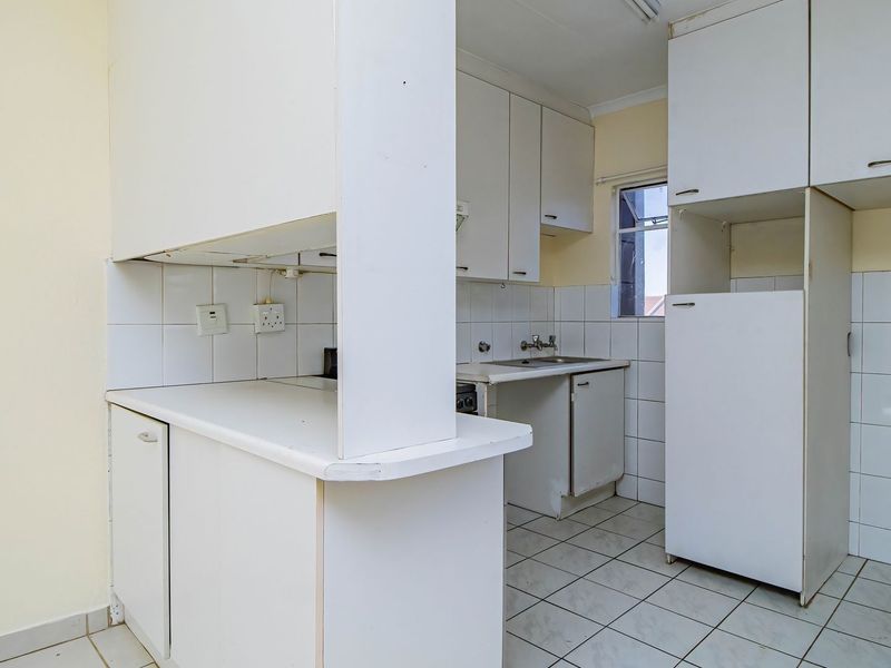 A functional, empty kitchen featuring white built-in cabinetry, tiled backsplash, and tiled flooring, offering a blank canvas for modern renovation.