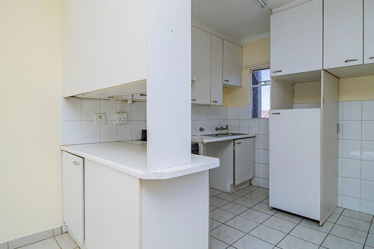 A functional, empty kitchen featuring white built-in cabinetry, tiled backsplash, and tiled flooring, offering a blank canvas for modern renovation.