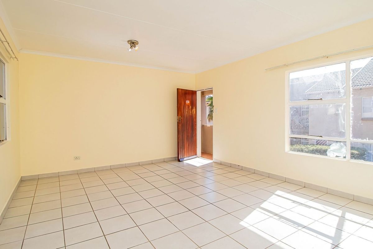 A bright, empty living room featuring neutral tiled flooring, large windows, and a timber entrance door, offering a clean canvas for interior design.