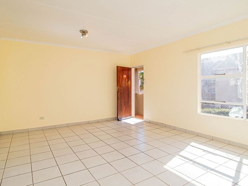 A bright, empty living room featuring neutral tiled flooring, large windows, and a timber entrance door, offering a clean canvas for interior design.