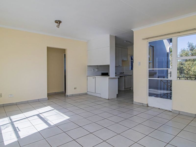 An open-plan living and kitchen area featuring neutral tiled flooring, built-in cabinetry, and direct access to an outdoor space through a glass door.