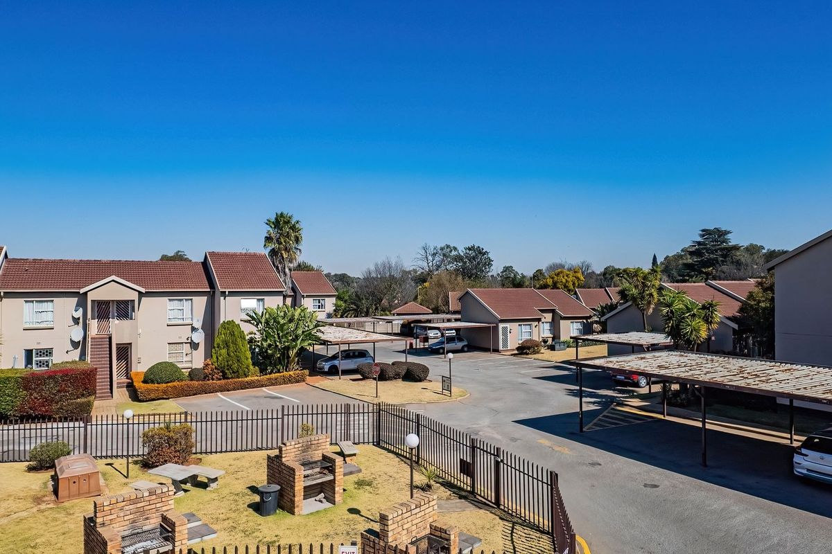 Aerial view of a residential flat complex featuring multiple buildings, covered parking bays, communal brick braai areas, and landscaped grounds.