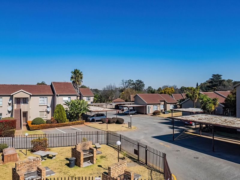Aerial view of a residential flat complex featuring multiple buildings, covered parking bays, communal brick braai areas, and landscaped grounds.