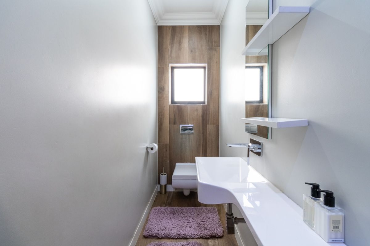 A modern, compact guest bathroom featuring a wall-mounted toilet, sleek floating vanity with integrated basin, and wood-look tile accents.