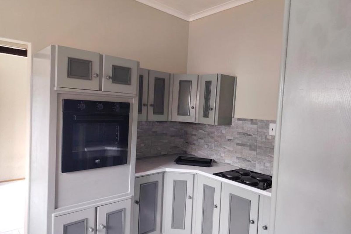 A compact kitchen featuring built-in cabinetry, a wall-mounted oven, and an electric hob with a tiled backsplash.