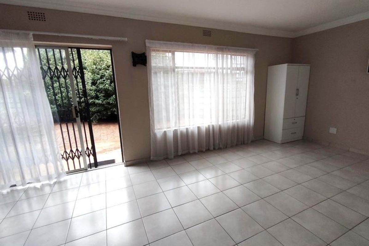 Spacious living area featuring neutral tiled flooring, large windows for natural light, and direct access to the outdoor patio through a sliding glass door.