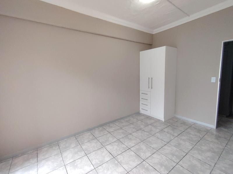 A clean, empty bedroom featuring neutral wall tones, tiled flooring, and a built-in white wardrobe.