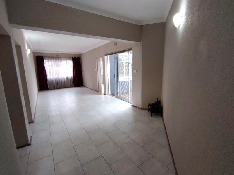 Spacious open-plan living area featuring neutral tiled flooring, ample natural light, and direct access to the outdoor area through a sliding glass door.