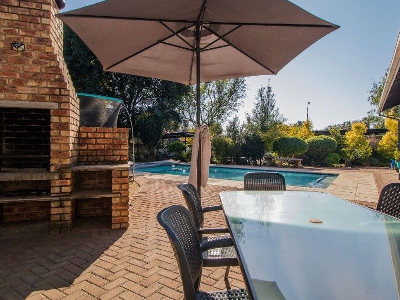 Outdoor patio area featuring a built-in brick braai, paved flooring, and direct access to a swimming pool in the garden.