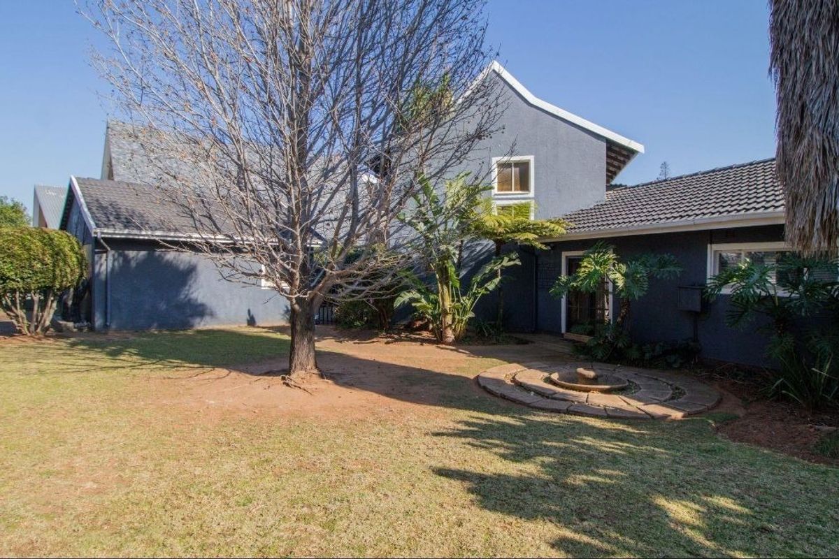 Rear view of the property featuring a spacious garden, mature trees, and a stone water feature set against the dark-painted exterior walls.