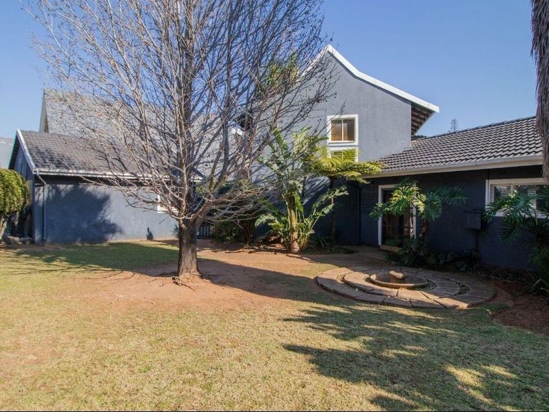 Rear view of the property featuring a spacious garden, mature trees, and a stone water feature set against the dark-painted exterior walls.