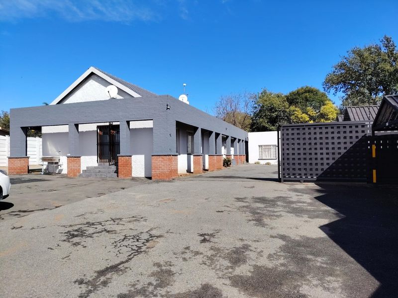 Front exterior view of the property featuring a large asphalt driveway, covered walkway with brick pillars, and secure perimeter fencing.