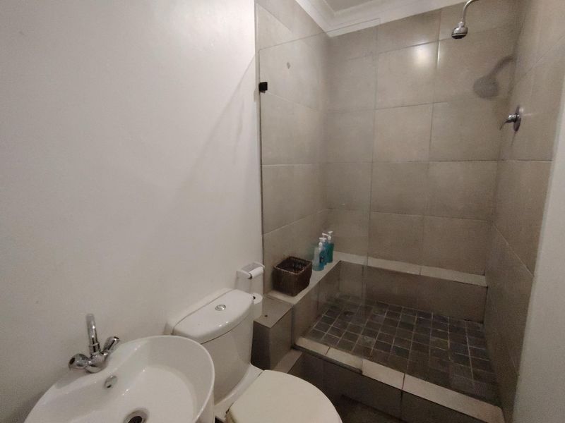 A functional bathroom featuring a walk-in shower with a glass screen, tiled flooring, a ceramic basin, and a standard toilet.