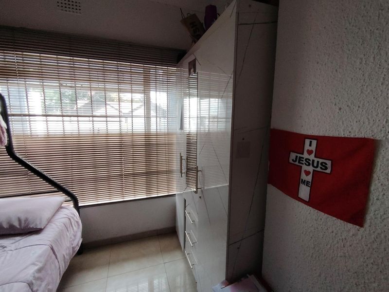 A bedroom featuring tiled flooring, a built-in wardrobe with a mirrored panel, and venetian blinds covering the window.