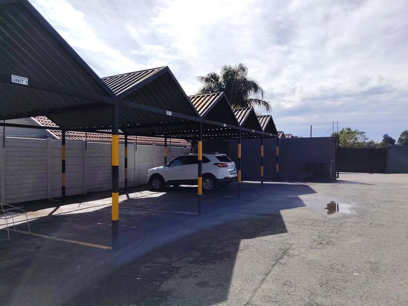 A well-maintained covered parking area featuring a metal roof structure and paved driveway, providing secure and protected vehicle storage.