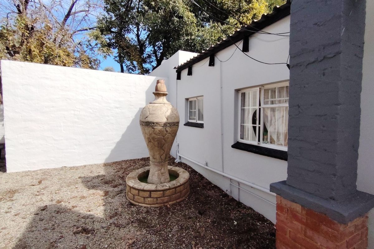 A private rear courtyard area featuring a decorative stone fountain, gravel landscaping, and a white masonry boundary wall adjacent to the main dwelling.