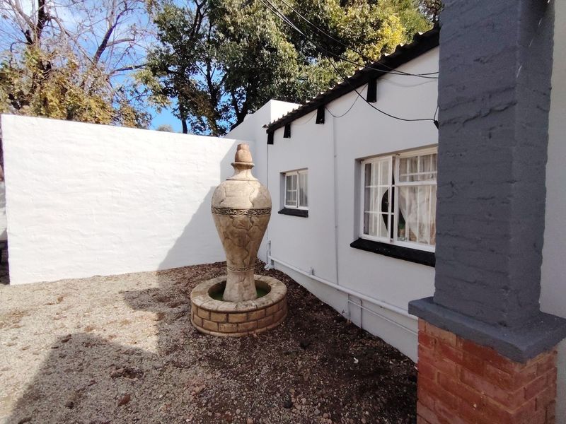 A private rear courtyard area featuring a decorative stone fountain, gravel landscaping, and a white masonry boundary wall adjacent to the main dwelling.