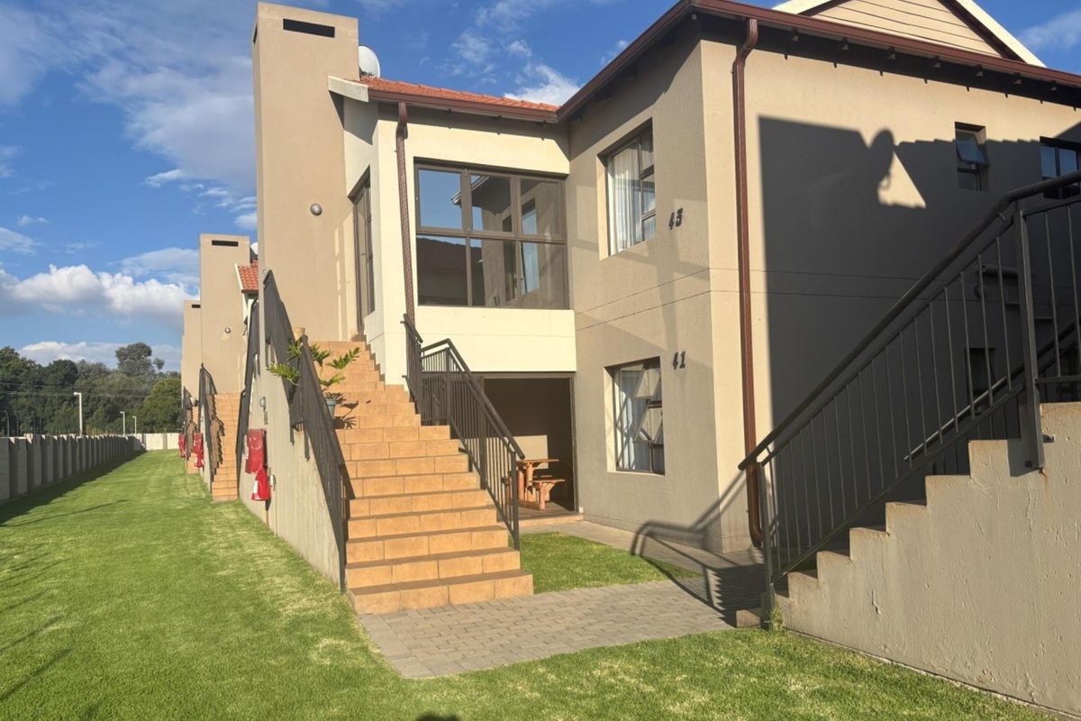 Exterior view of a multi-level apartment complex featuring tiled staircases, metal railings, and a well-maintained lawn area.