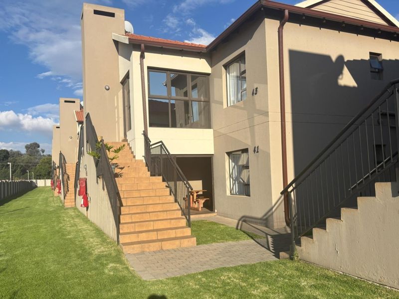 Exterior view of a multi-level apartment complex featuring tiled staircases, metal railings, and a well-maintained lawn area.