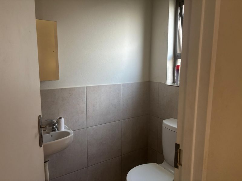 A compact bathroom featuring a wall-mounted basin, toilet, and neutral wall tiling, providing a functional and clean space.