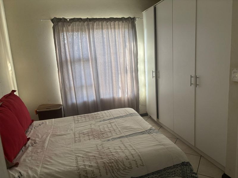 A bedroom featuring tiled flooring and a large white built-in wardrobe with modern handles.