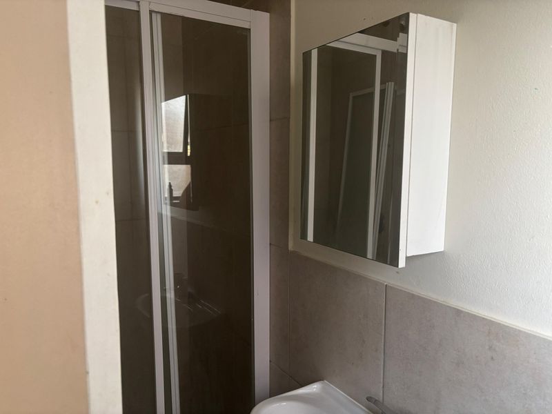 A functional bathroom featuring a shower enclosure, a wall-mounted basin, and a mirrored medicine cabinet with neutral wall tiling.