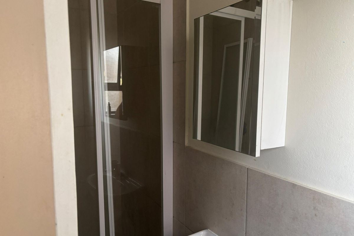A functional bathroom featuring a shower enclosure, a wall-mounted basin, and a mirrored medicine cabinet with neutral wall tiling.