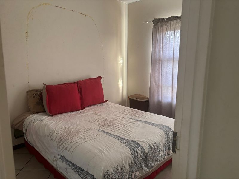 A bedroom featuring tiled flooring and a window, currently showing signs of wall surface wear and paint damage.