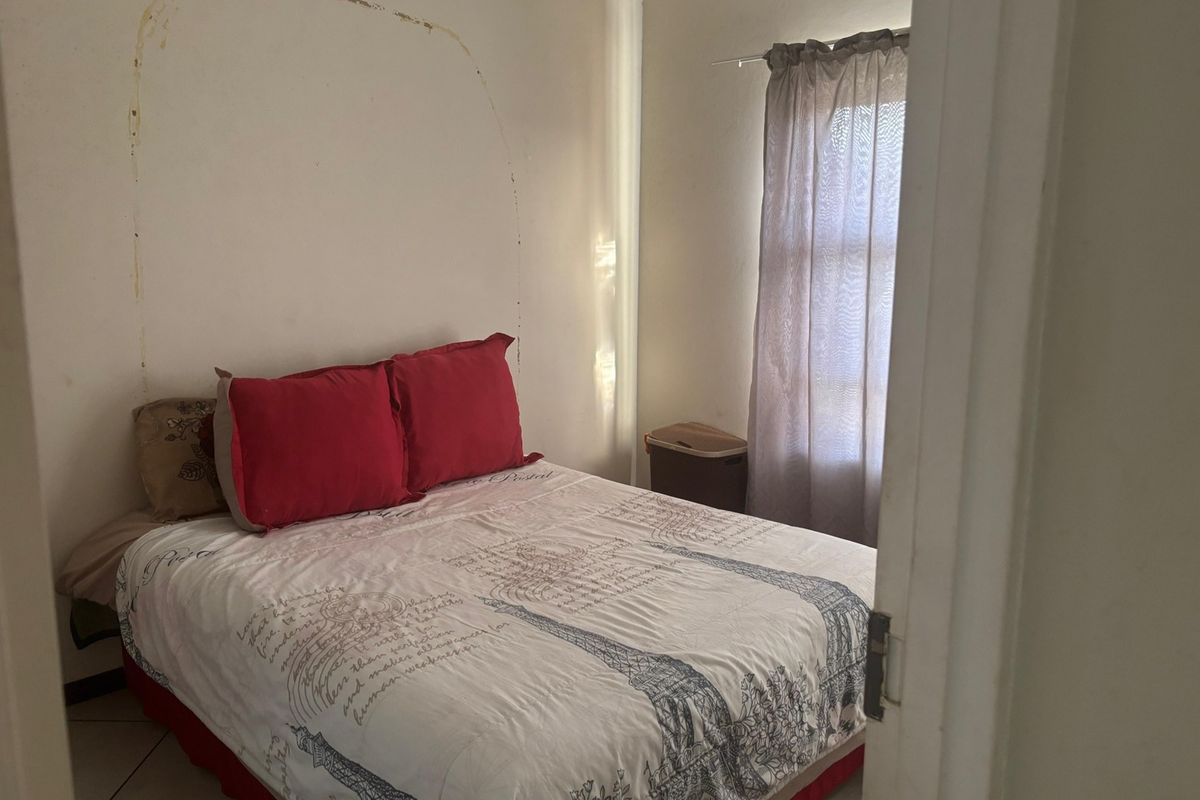 A bedroom featuring tiled flooring and a window, currently showing signs of wall surface wear and paint damage.